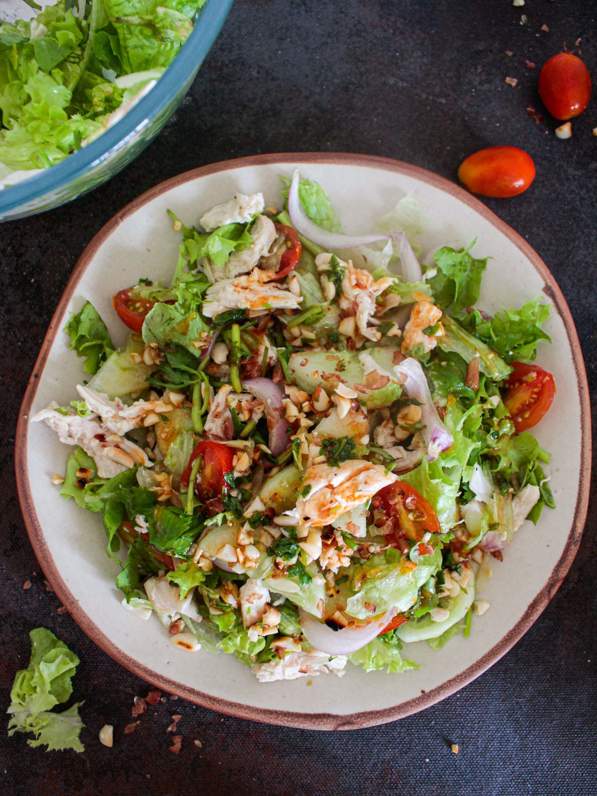 brown and white bowl of thai chicken salad on black table