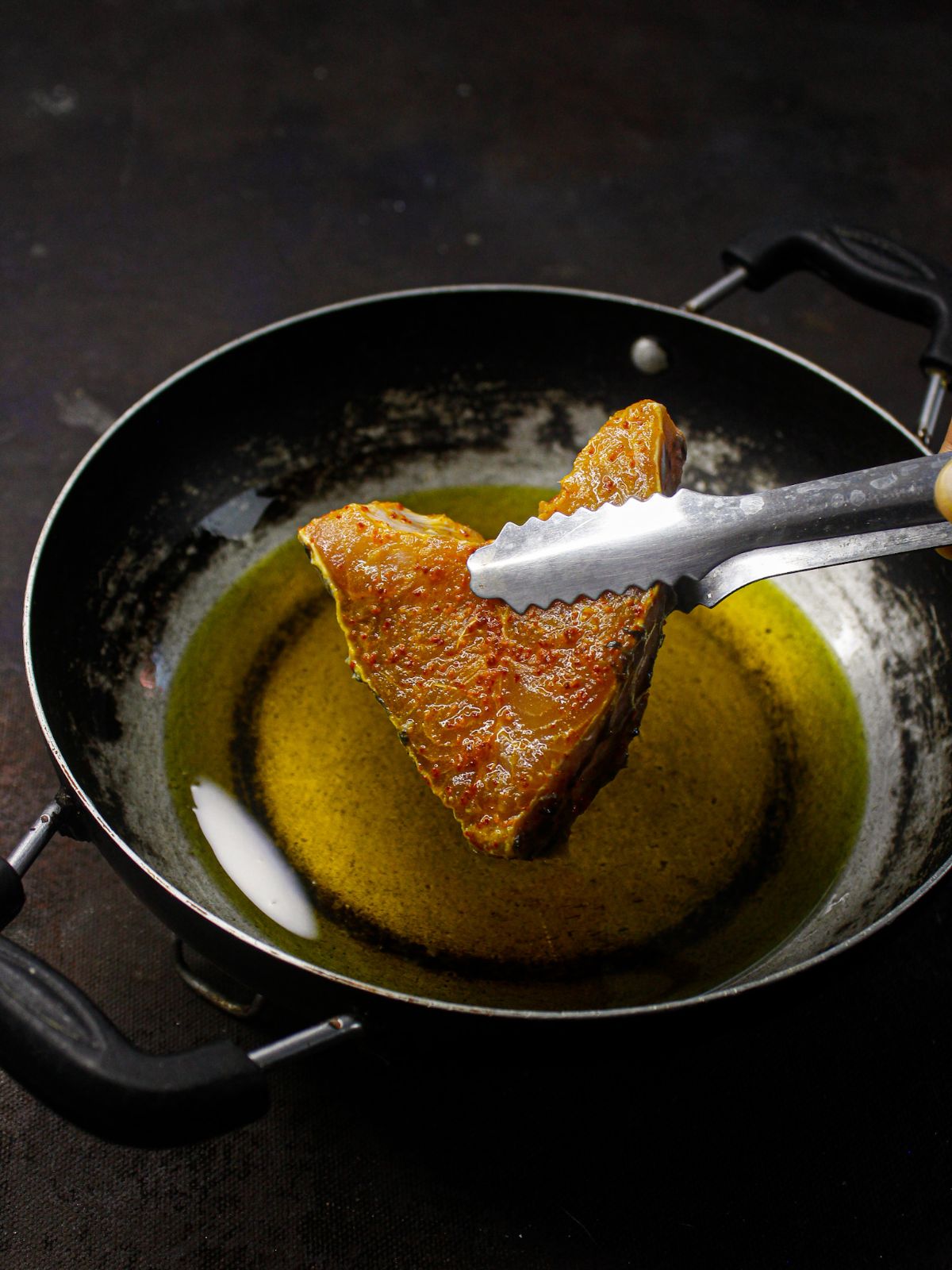 tongs holding fish over hot oil
