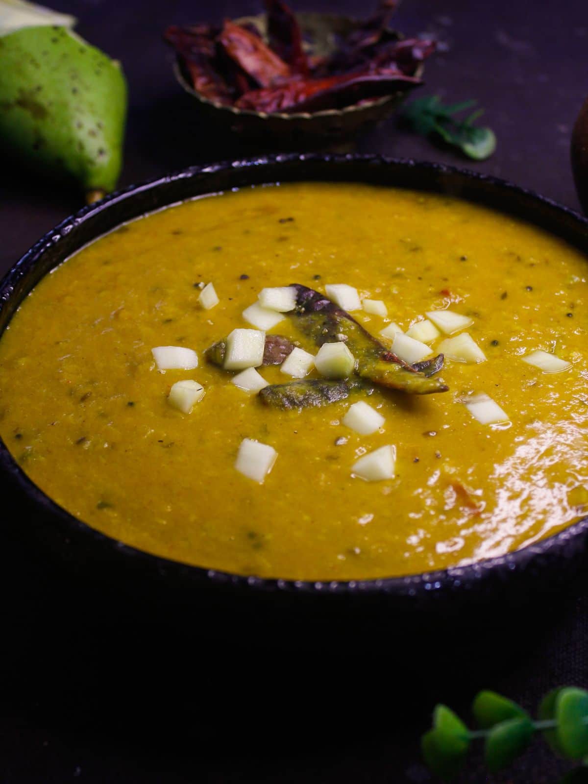 large black bowl of mango dal on table by green chile